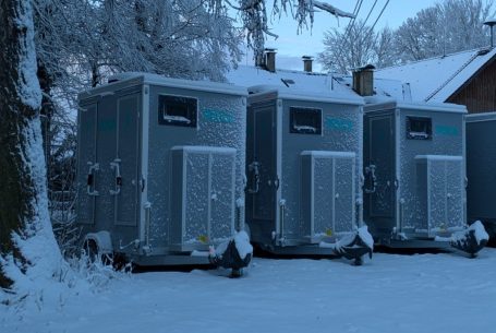 Drei graue mobile Toiletten Anhänger in einer verschneiten Landschaft.